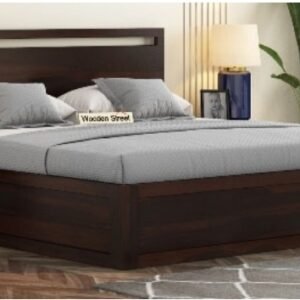 Dark wood platform bed with gray bedding and multiple pillows in a modern bedroom, with nightstands, a lamp, a plant, and a patterned rug visible.